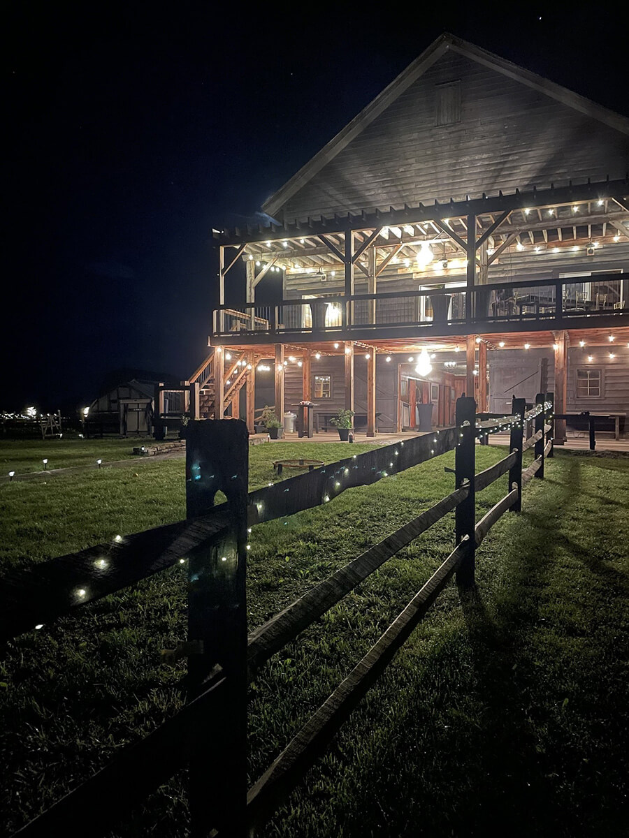 Rustic barn deck overlooking scenic field with tents and a wood fence.