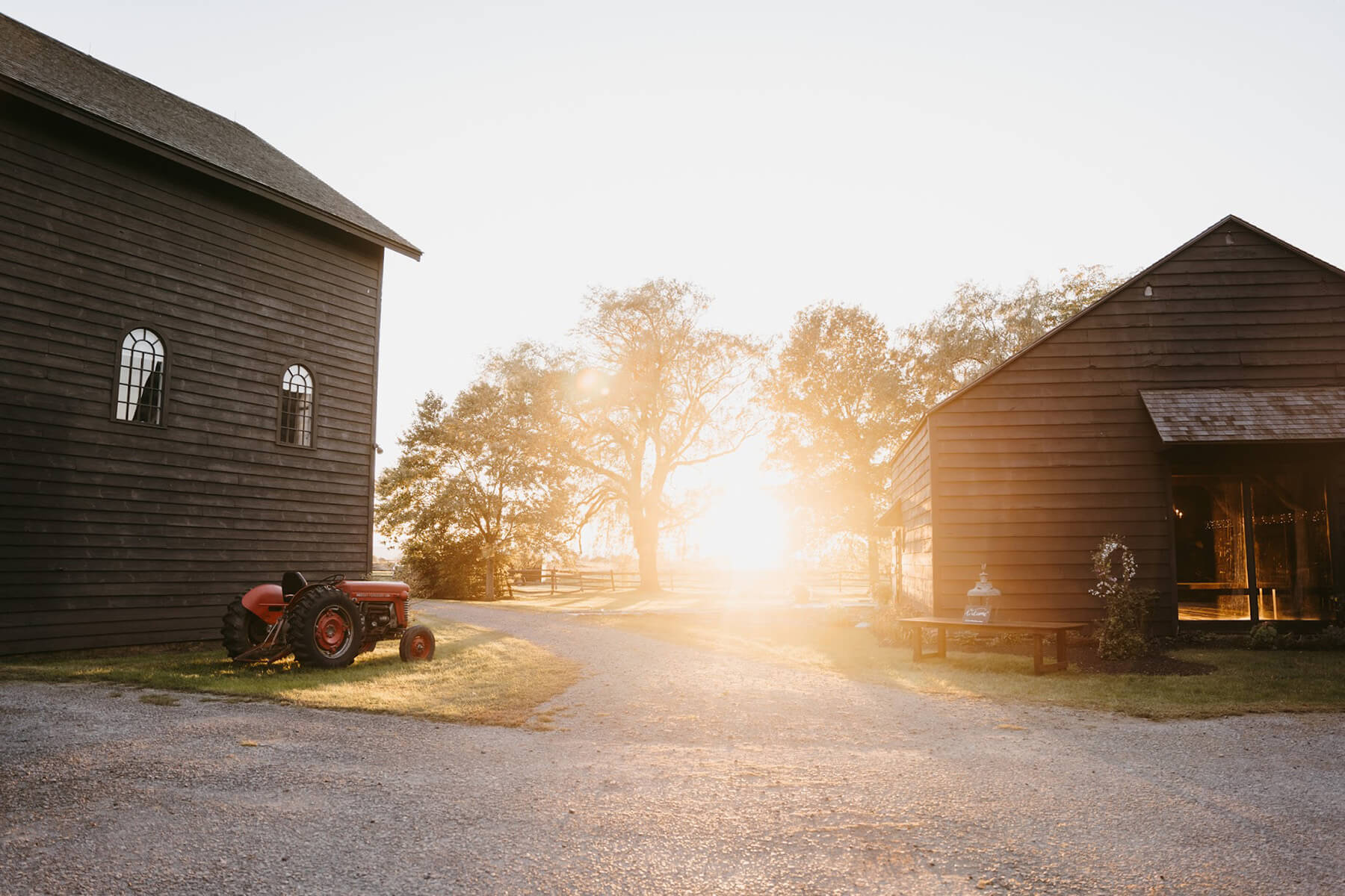 Scenic wedding venue during sunset with rustic tractor and barn buildings.